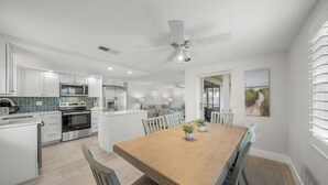 A modern kitchen with white cabinetry, a wooden dining table, and a ceiling fan.