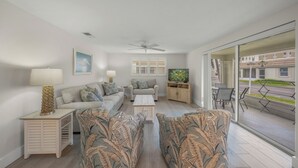 A modern living room with a sofa set, a coffee table, a TV, and a balcony with outdoor furniture.