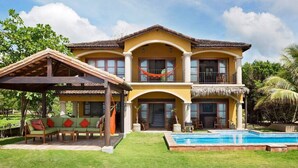 Ein zweistöckiges Haus mit Pool, Sitzgelegenheiten im Freien und einem Strohdach.
