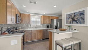 A modern kitchen with wooden cabinets, a stainless steel refrigerator, and a large island with stools. - Island House Beach Resort V1 (Siesta Key)