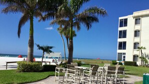A patio area with outdoor seating, palm trees, and a view of the beach and ocean. - Island House Beach Resort V1 (Siesta Key)