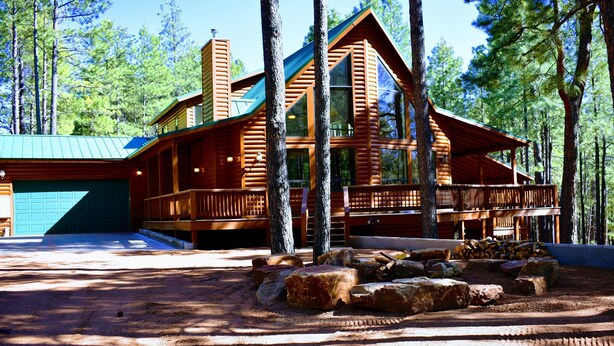A log cabin with a large porch, a garage, and a stone fireplace.