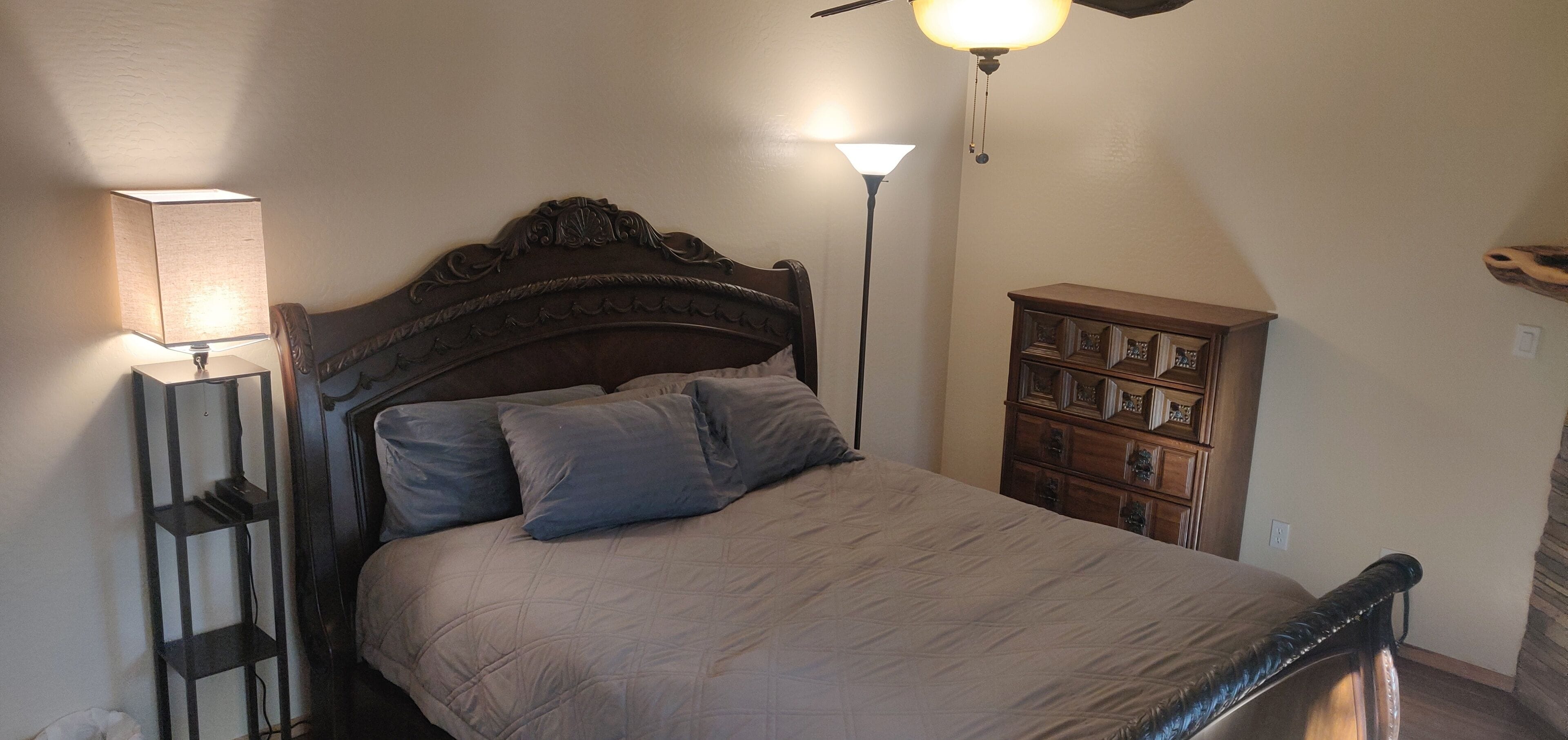 A bedroom with a bed, bedside lamps, a nightstand, and a wooden dresser.