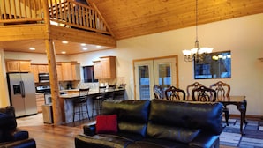 A spacious living area with a leather sofa, wooden flooring, a kitchen with wooden cabinets, and a dining area with a wooden table and chairs.