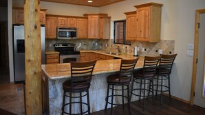 A kitchen with wooden cabinets, a granite countertop, a built-in microwave, and a stainless steel refrigerator.