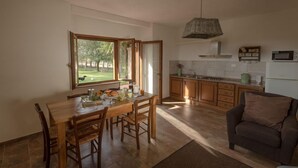 A dining area with a wooden table and chairs, a kitchen with wooden cabinets, and a view of a park through large windows. - Agritiurismo San Carlo-Family apartment - 3 bedrooms with San Carlo Quadri pool (pomarance)