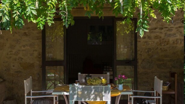 An outdoor patio with a table set for two, surrounded by wicker chairs. A table with a yellow tablecloth holds a fruit bowl, a vase with flowers, and a pitcher. - Agritiurismo San Carlo-Family apartment - 3 bedrooms with San Carlo Quadri pool (pomarance)