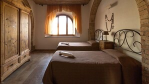 A room with two beds, a wooden wardrobe, a window with curtains, and a wall-mounted lamp. - Agritiurismo San Carlo-Family apartment - 3 bedrooms with San Carlo Quadri pool (pomarance)