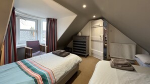 Ein Schlafzimmer mit zwei Betten, einem Schreibtisch, einem Stuhl, einem Heizkörper und einem Fenster mit Vorhängen.