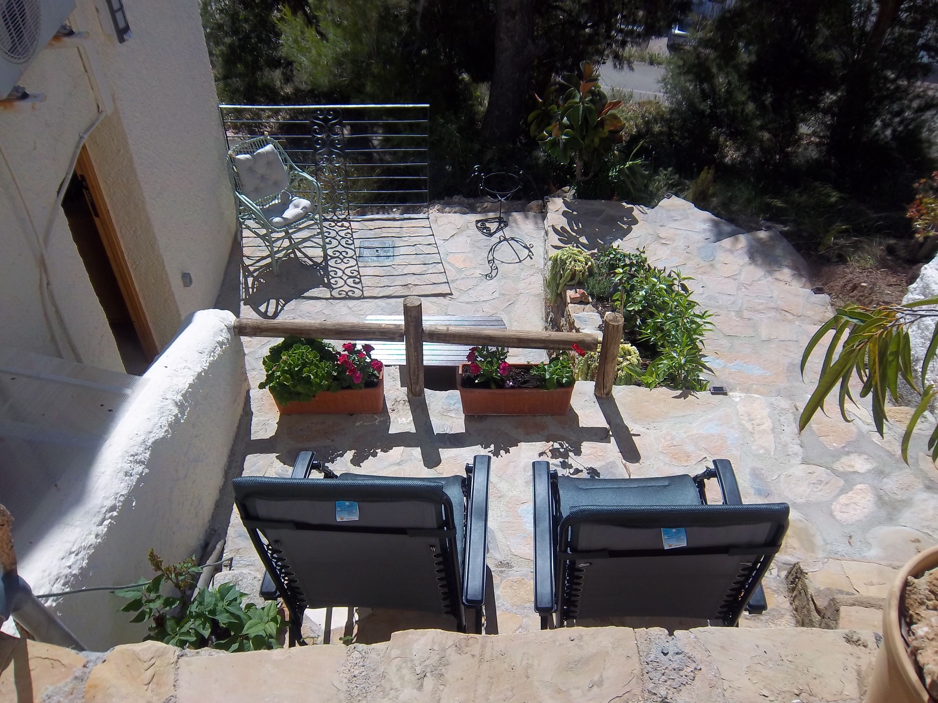 Un patio de piedra con dos sillones negros, una mesa metálica y plantas en macetas.