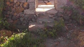 Une construction en pierre avec une porte d’entrée donnant sur une pièce où se trouvent une chaise jaune et un lit.