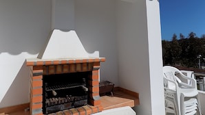 An outdoor brick grill under a white pergola, with white plastic chairs and a clear blue sky in the background. - Stunning Villa with Private Garden, Shared Pool, 10 min from lovely beach (Foz do Arelho)
