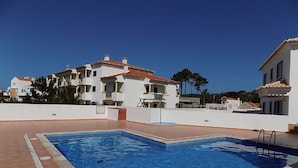 A swimming pool with a tiled deck, surrounded by a white building with balconies and a red-tiled roof. - Stunning Villa with Private Garden, Shared Pool, 10 min from lovely beach (Foz do Arelho)