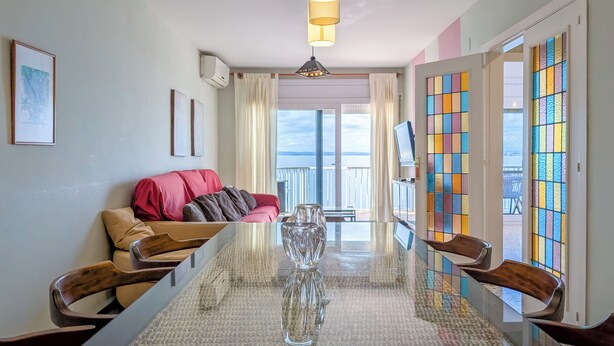 Uma sala de estar moderna com uma mesa de jantar de vidro, um sofá vermelho e vista para o exterior.