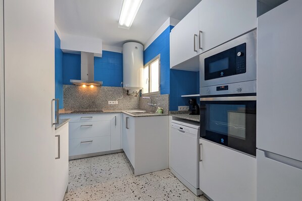 A compact kitchen with white cabinets, a built-in oven, and a microwave. - Agi Avenida 5B Apartamento for rent in Roses Girona. (Rosas / Roses)
