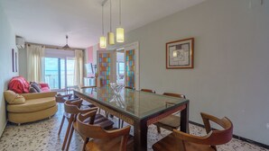 Uma sala de jantar com uma mesa de vidro, cadeiras de madeira, um sofá vermelho e vista pela janela.