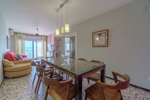 Un coin repas avec une table à plateau en verre, des chaises en bois, un canapé rouge et une vue par la fenêtre.