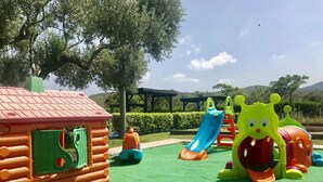 Un'area giochi con una casetta di legno, scivoli e un’attrezzatura giochi a forma di bruco.