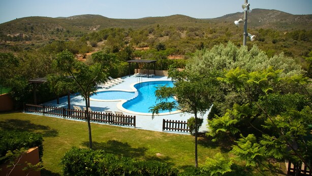 Una piscina con bordo in legno e lettini, circondata da vegetazione e colline sullo sfondo.