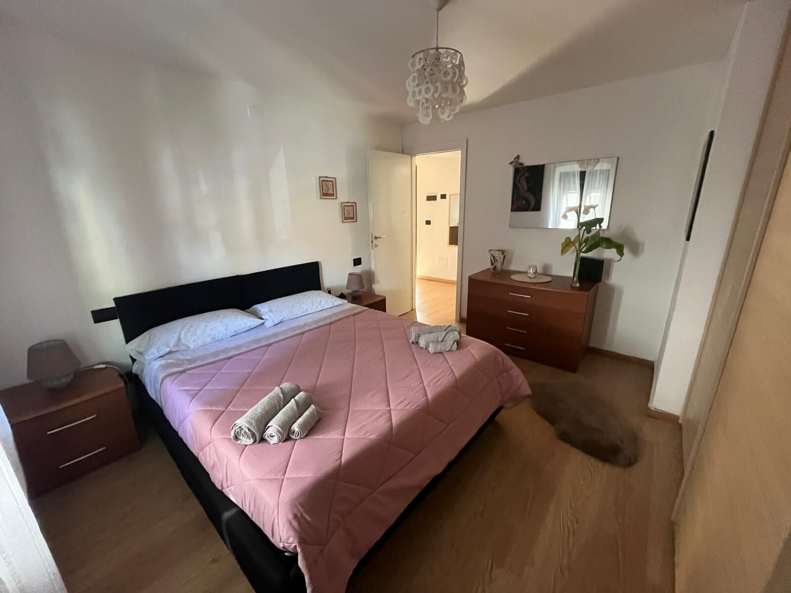 A bedroom with a bed, bedside tables, a dresser, a mirror, and a hanging light fixture.
