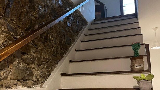 Un escalier avec un mur en pierre d’un côté et une main courante en bois. Les marches mènent à un palier où se trouve une petite plante en pot et un objet décoratif portant l’inscription « sweet ».