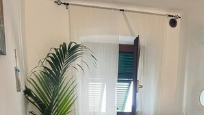 Une cuisine avec un plan de travail en bois foncé, une grande plante verte, un pot décoratif en pierre et une fenêtre ornée de rideaux blancs.