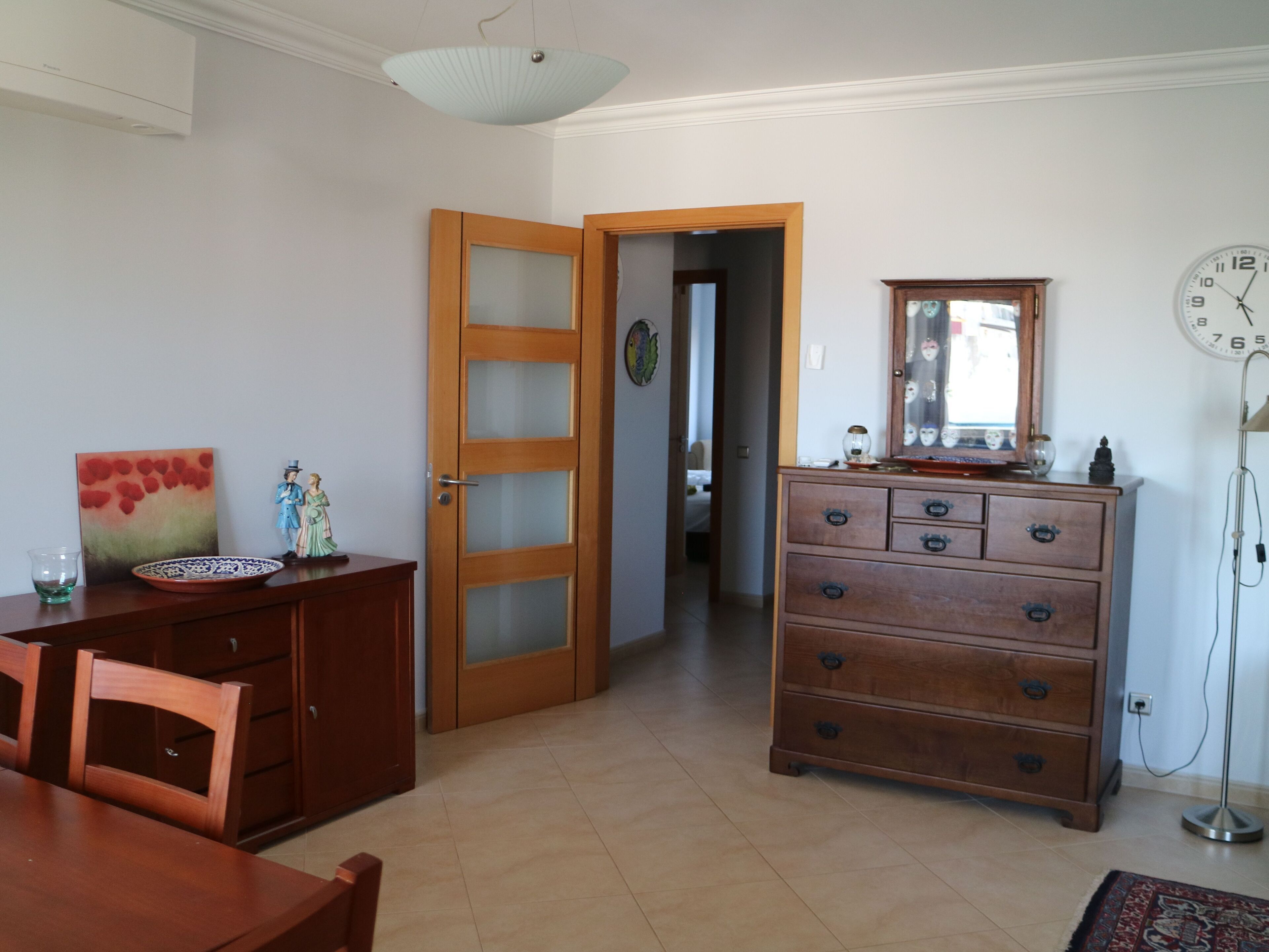 Una habitación con un aparador de madera, una mesa de comedor con sillas, un cuadro y un reloj en la pared.
