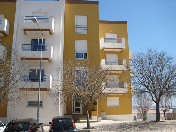A multi-story residential building with balconies, a parking area, and leafless trees. - 3 bedrooms, 50 m2 private terrace, air conditioned all rooms, renovated 2022 (Tavira)