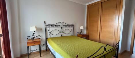 A bedroom with a bed, two bedside tables with lamps, a wooden wardrobe, and a wooden floor.