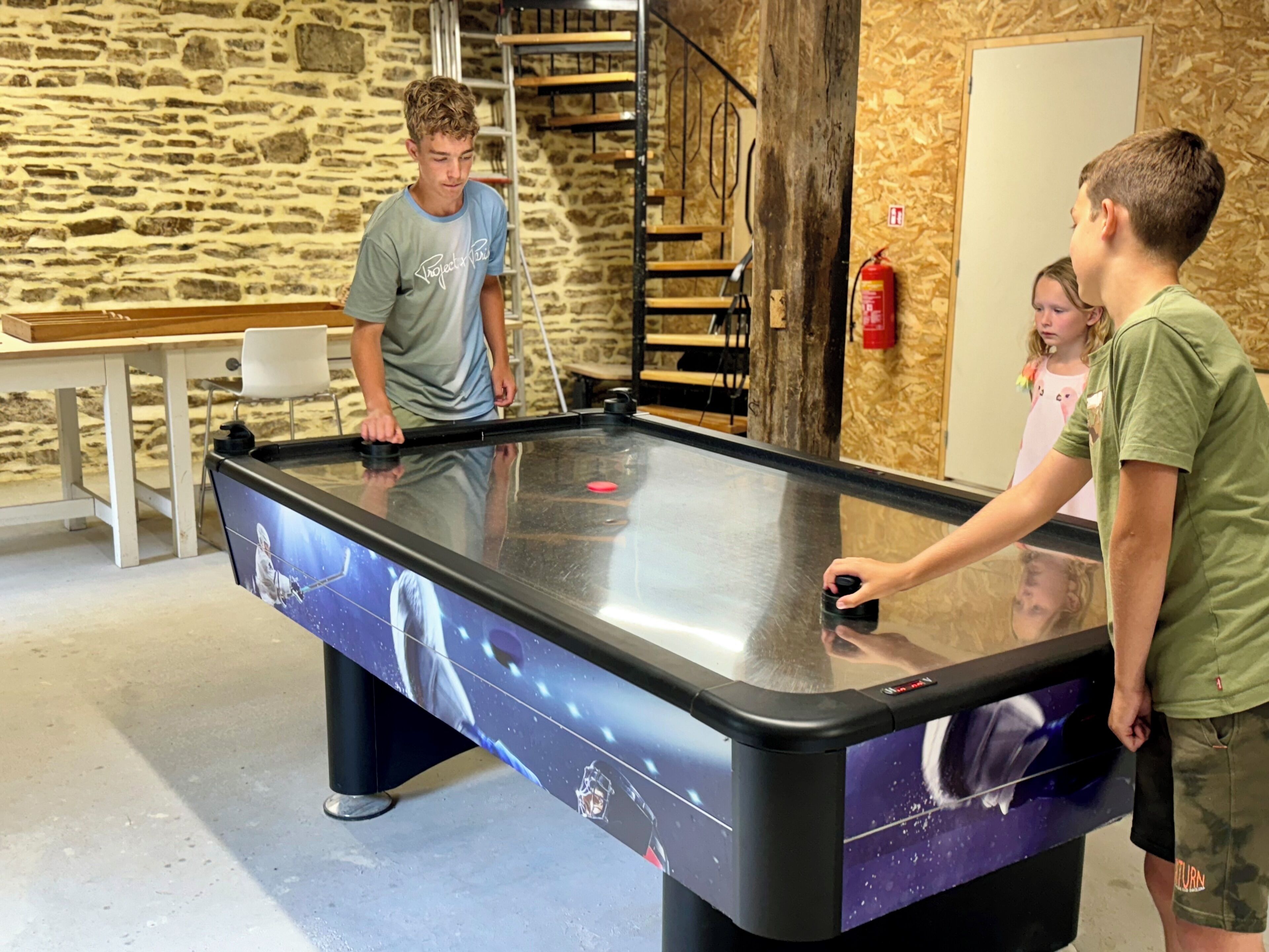 Une table de billard au design inspiré de l’espace, un mur en pierre et un escalier en bois en arrière-plan.