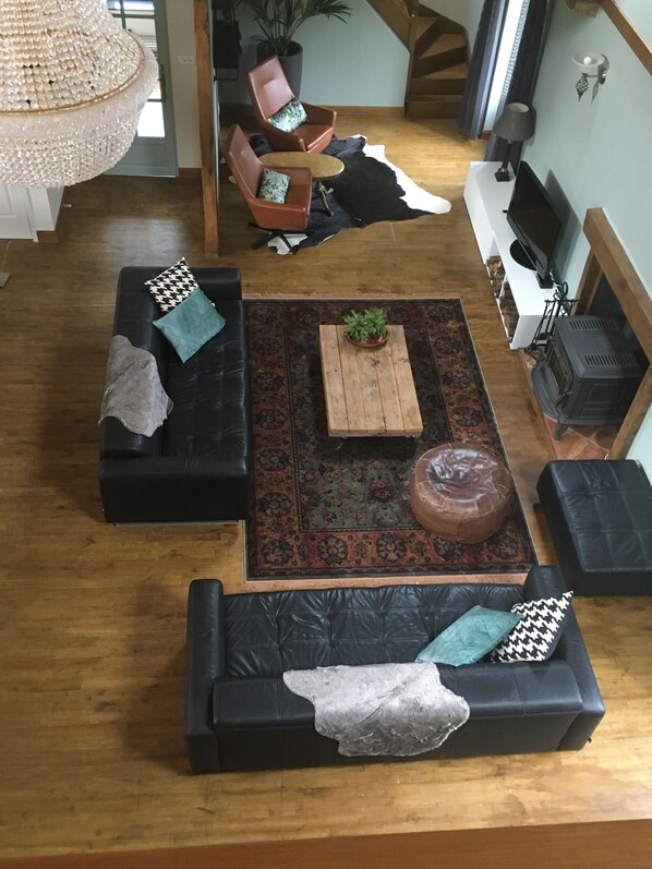 A spacious living room with a large wooden coffee table, two black leather sofas with patterned cushions, a wooden floor, and a decorative rug. - Spacious luxury Watermill |14-20 pers | Mont St Michel | forest | child friendly (Saint James)