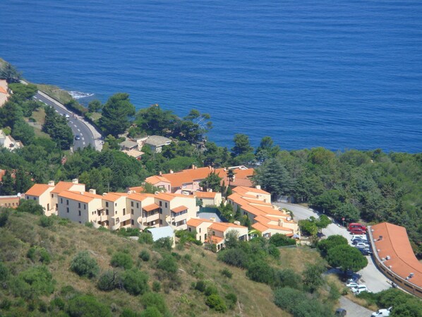 A coastal residential area with terraced houses, a road, and parked cars.