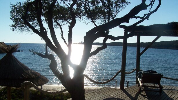 A wooden deck with a bench and a rope barrier, overlooking a body of water with a thatched structure in the background. - house / villa - Monacia d'Aullène (Monacia-D'aullène)