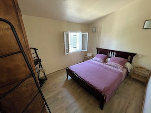 A bedroom with a bed, a window, a nightstand, and a wooden ladder.