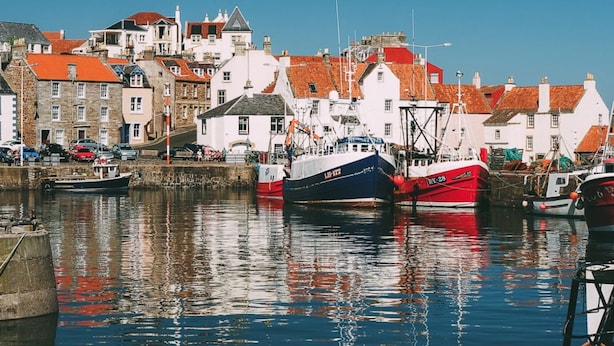 A harbor with boats docked, buildings with red roofs, and a clear blue sky. - A delightful and historic property just a few steps from the harbour. (Pittenweem)