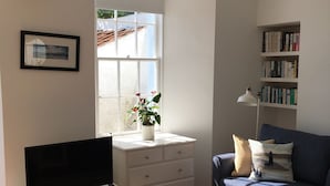 A living room with a TV, a sofa, a bookshelf, a window with a view, and a potted plant. - A delightful and historic property just a few steps from the harbour. (Pittenweem)