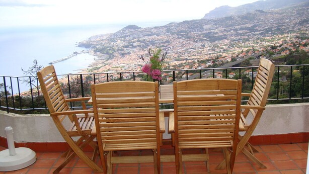 A wooden table and chairs on a balcony with a view of a coastal city.