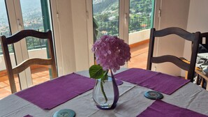 A table set with purple placemats, a vase with a hydrangea, and a view of a mountainous landscape through a glass door.