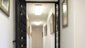 Een gang met houten vloeren, een decoratieve zwarte metalen poort en lijstwerken op de muren.