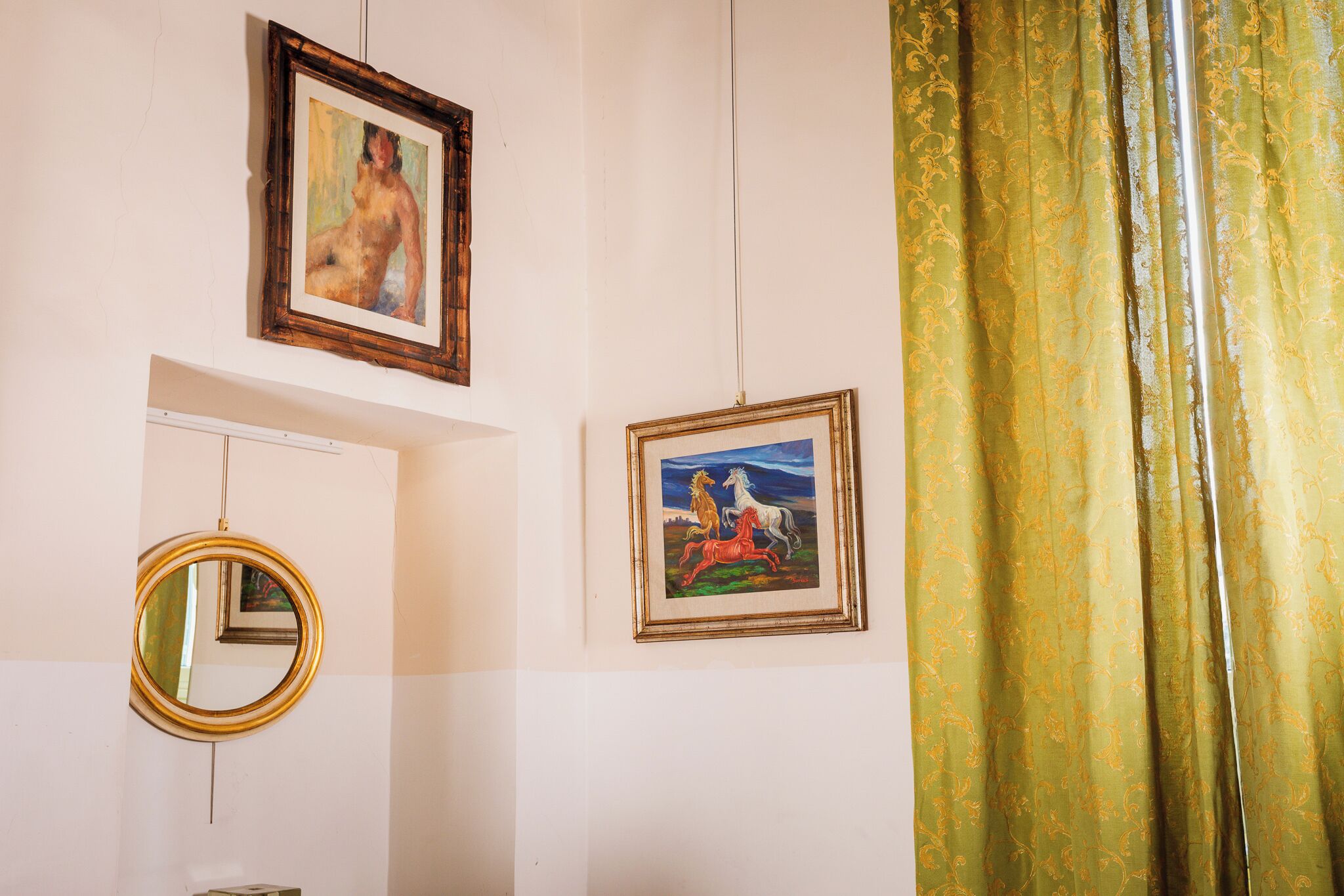 A room with a white wall, a framed painting of a horse, a mirror, and a curtain.