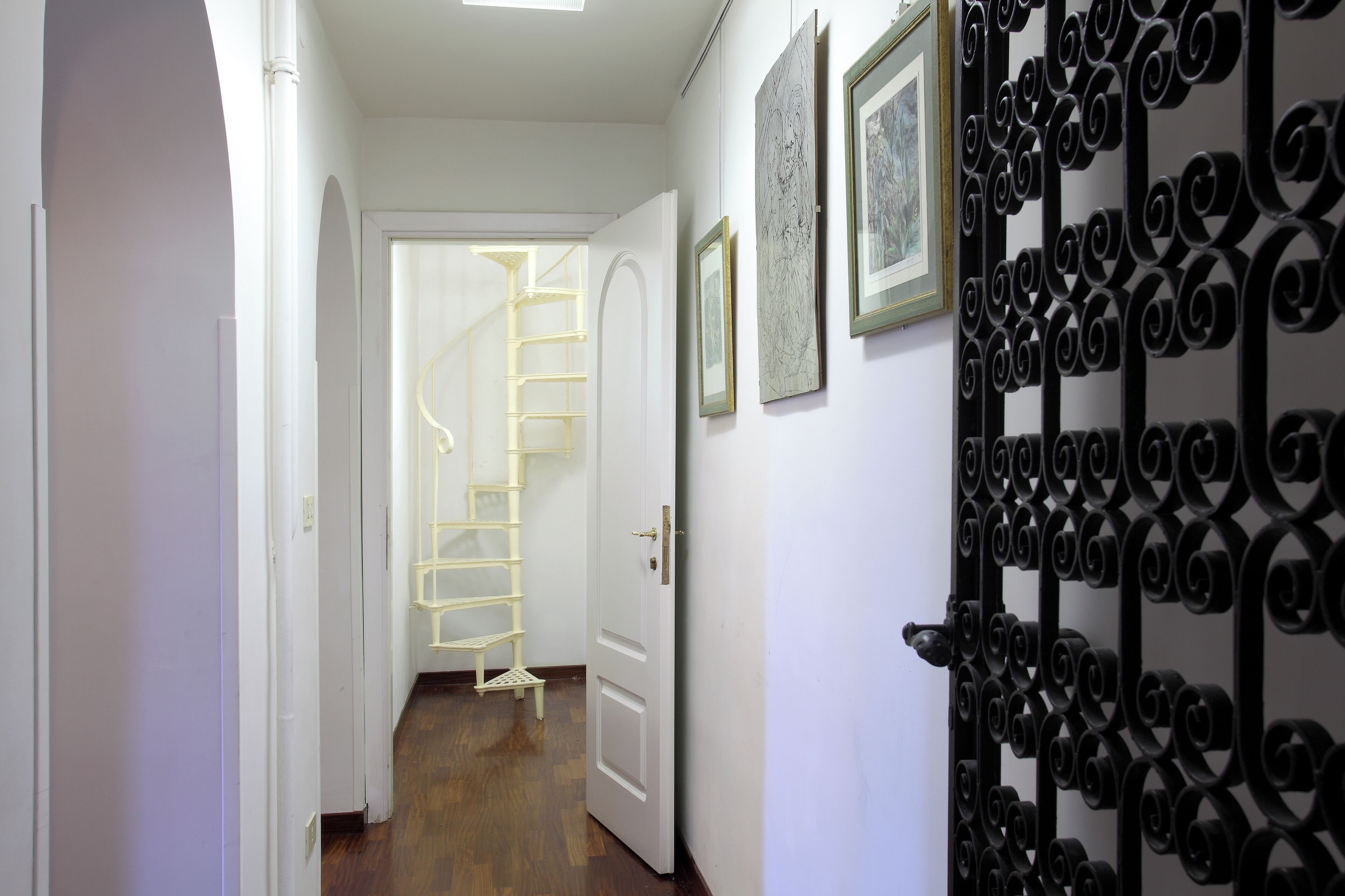 A hallway with a white door, a black decorative gate, and a spiral staircase leading to another room.