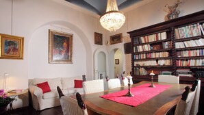 Een eethoek met een houten tafel, stoelen, een kroonluchter en een boekenkast vol boeken.