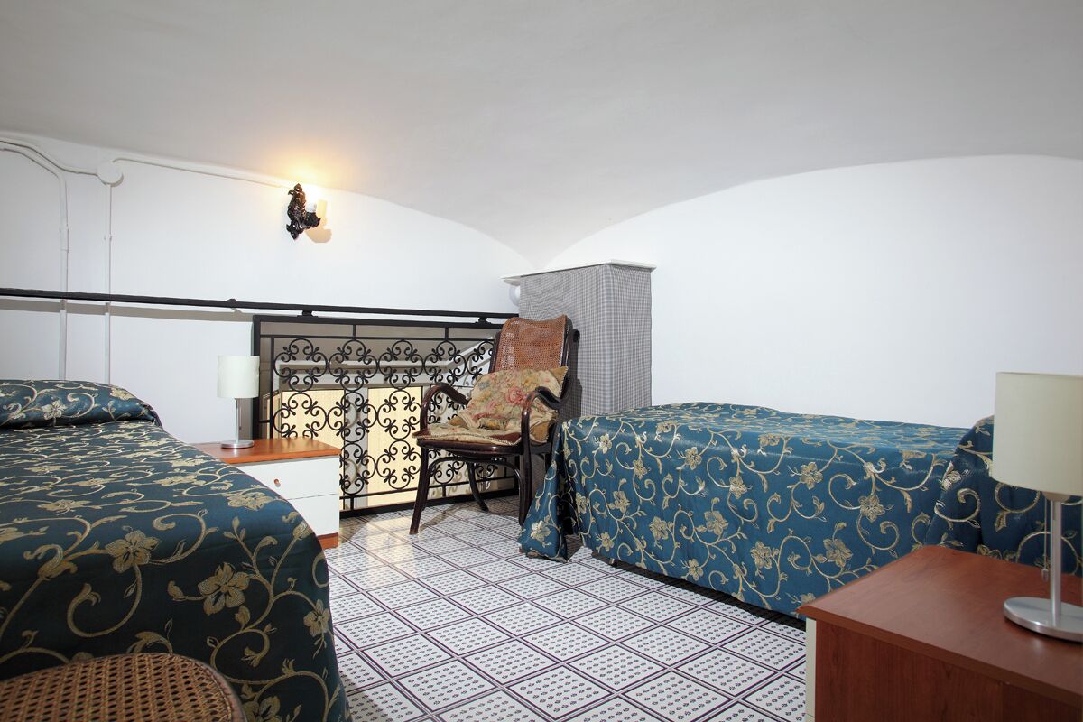 Ein Hotelzimmer mit zwei Betten, einem Sessel, einem Schreibtisch und einer Lampe.