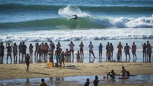 Una platja amb gent mirant un surfista surant una ona.
