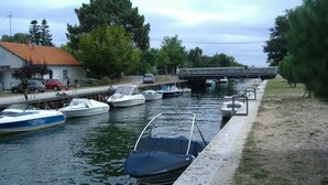 Un canal amb barques amarrades als laterals, un pont al fons i una zona verda a la dreta.