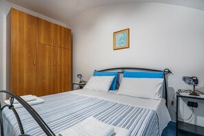 A bedroom with a bed, wooden wardrobe, bedside tables, and a wall-mounted picture.