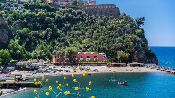 A coastal town with a prominent castle on a hill, a beach with boats, and a pier with buildings. - Domus Le Postali, Lovely 2 bedroom beach apartment on Sorrento Coast (Vico Equense)