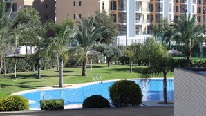 Una piscina rodeada de palmeras y follaje, con edificios altos al fondo.
