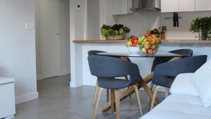Una cocina moderna con armarios blancos, una isla central con un cuenco de fruta y un comedor con un sofá blanco y dos sillas.