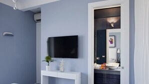 A modern bathroom with a large mirror, a sink, and a toilet. There is a flat-screen TV mounted on the wall above the mirror.